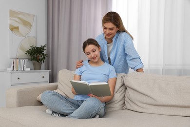 Happy mother and her teenage daughter spending time together with book at home