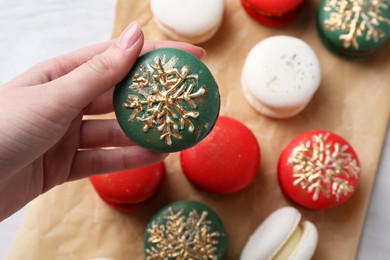 Photo of Woman with decorated Christmas macaron at table, closeup