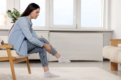 Photo of Woman suffering from leg pain on armchair at home, space for text
