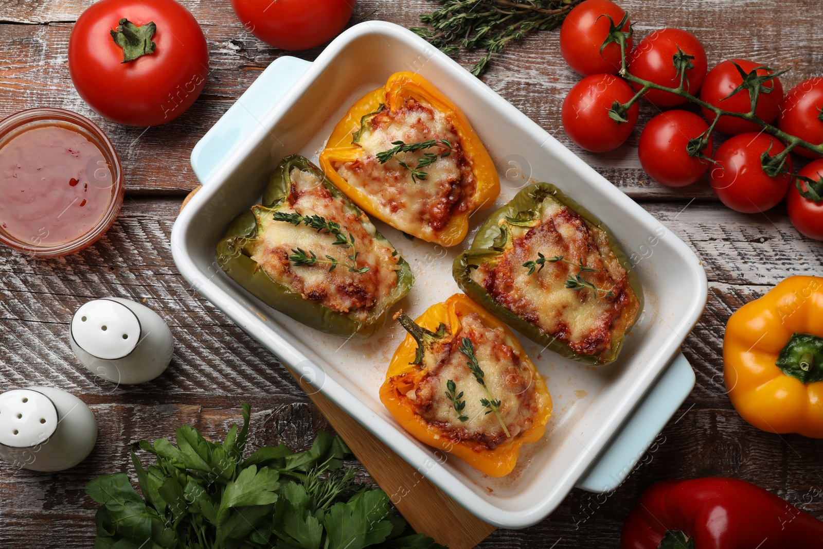 Photo of Tasty stuffed peppers in dish and ingredients on wooden table, flat lay