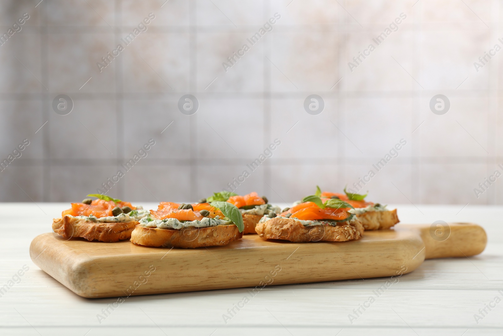Photo of Tasty canapes with salmon, capers and sauce on white wooden table, space for text