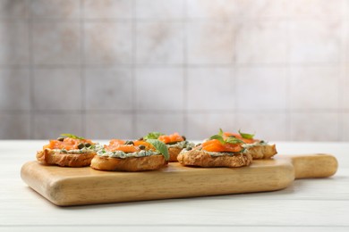 Photo of Tasty canapes with salmon, capers and sauce on white wooden table, space for text
