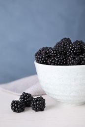 Photo of Fresh ripe blackberries in bowl on white table against blue background