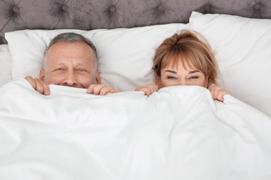 Photo of Mature couple hiding together under blanket in bed at home