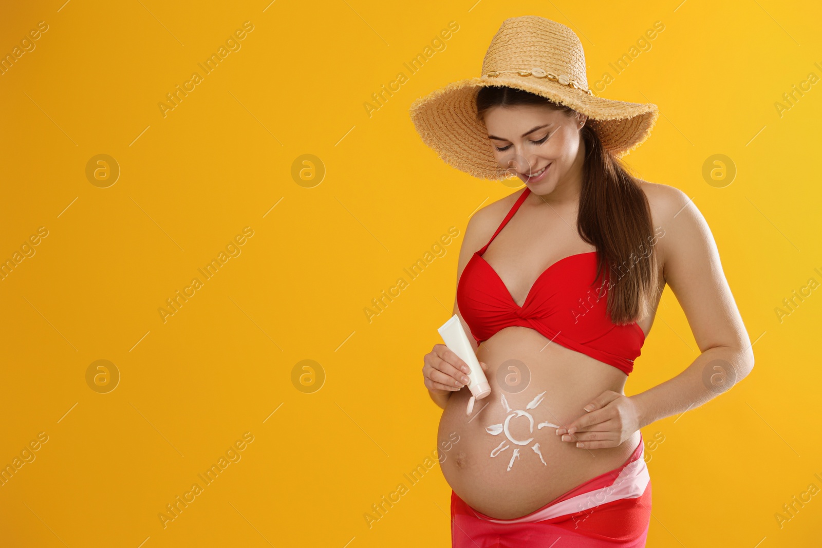 Photo of Young pregnant woman with sun protection cream on yellow background, space for text