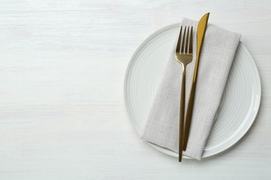 Stylish ceramic plate, cutlery and napkin on white wooden table, top view. Space for text