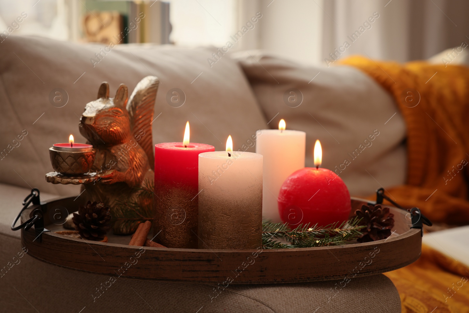 Photo of Tray with beautiful burning candles and Christmas decor on sofa at home