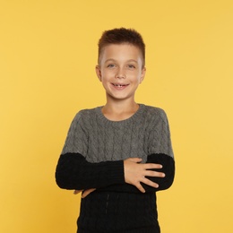 Photo of Cute little boy in warm sweater on yellow background. Winter season