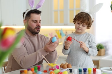 Photo of Easter celebration. Father with his little son painting eggs at table in kitchen