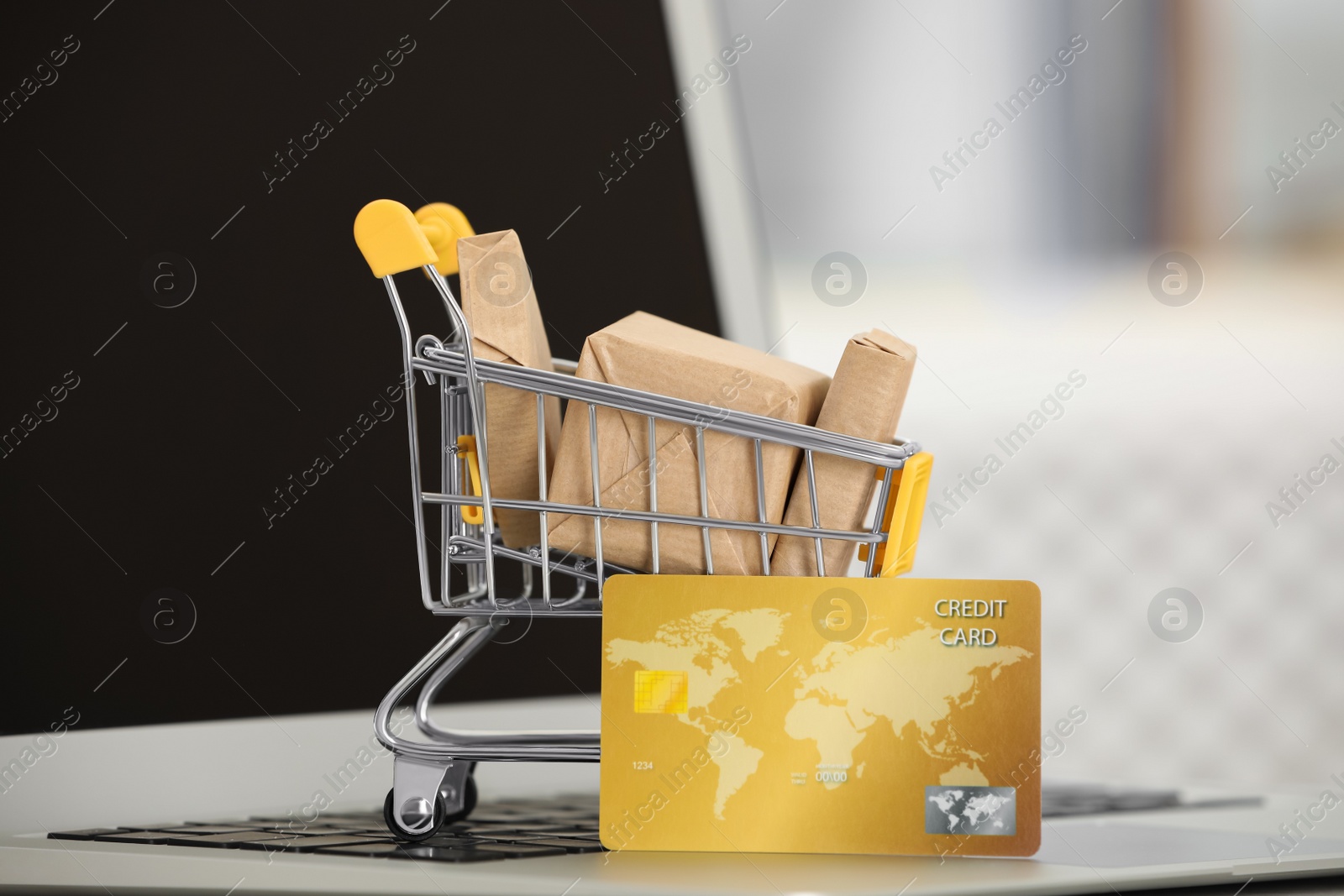 Photo of Online payment concept. Small shopping cart with bank card, boxes on laptop, closeup