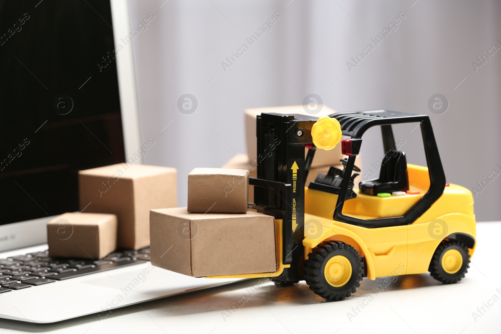 Photo of Toy forklift with boxes near laptop on table. Logistics and wholesale concept