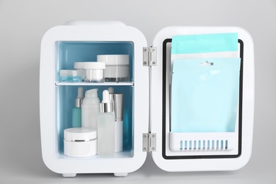 Photo of Open cosmetic refrigerator with skin care products on light background