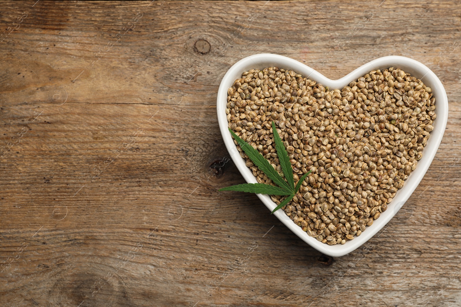 Photo of Organic hemp seeds and leaf on wooden background, top view. Space for text