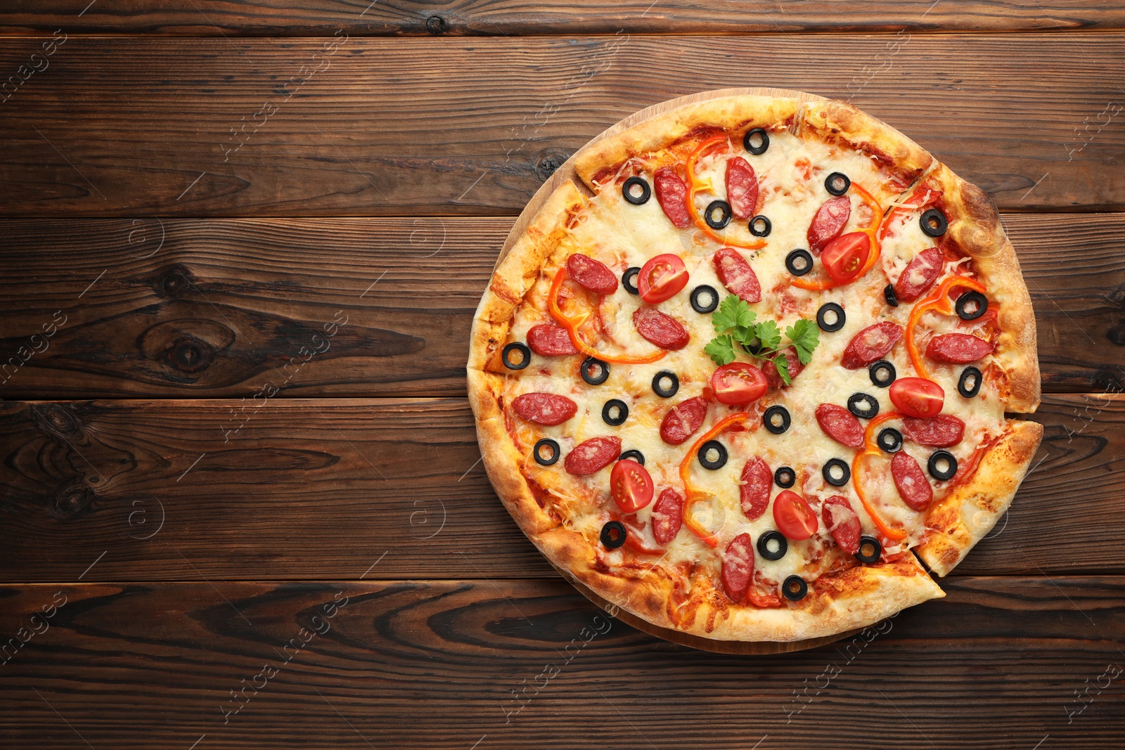Photo of Tasty pizza with dry smoked sausages, tomato, olives, pepper and parsley on wooden table, top view. Space for text