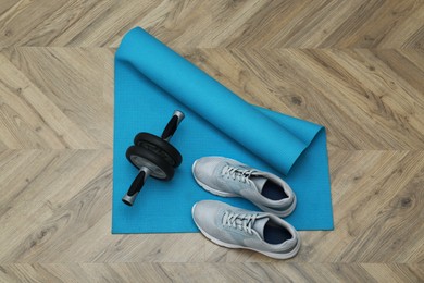 Photo of Exercise mat, ab roller and shoes on wooden floor, top view