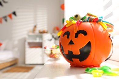 Photo of Halloween trick or treat bucket with different sweets near window indoors