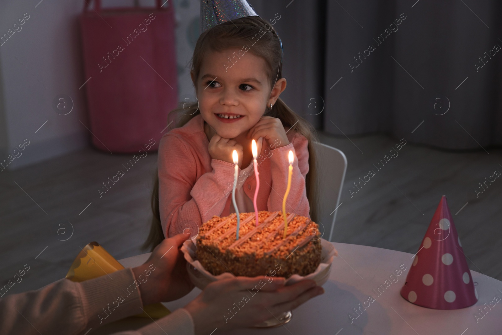 Photo of Birthday celebration. Mother holding tasty cake with burning candles near her daughter indoors