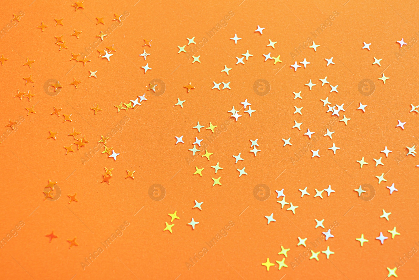 Photo of Shiny bright glitter on orange background, top view