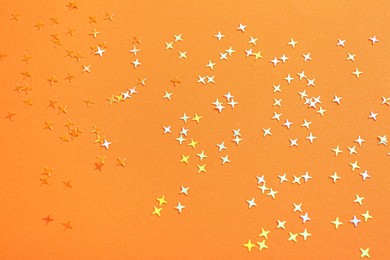 Photo of Shiny bright glitter on orange background, top view