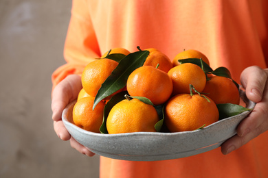 Photo of Woman holding bowl of tangerines, closeup. Juicy citrus fruit