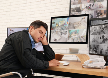 Photo of Male security guard sleeping near monitors at workplace