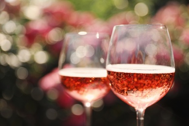 Photo of Glasses of rose wine in blooming garden, closeup. Space for text