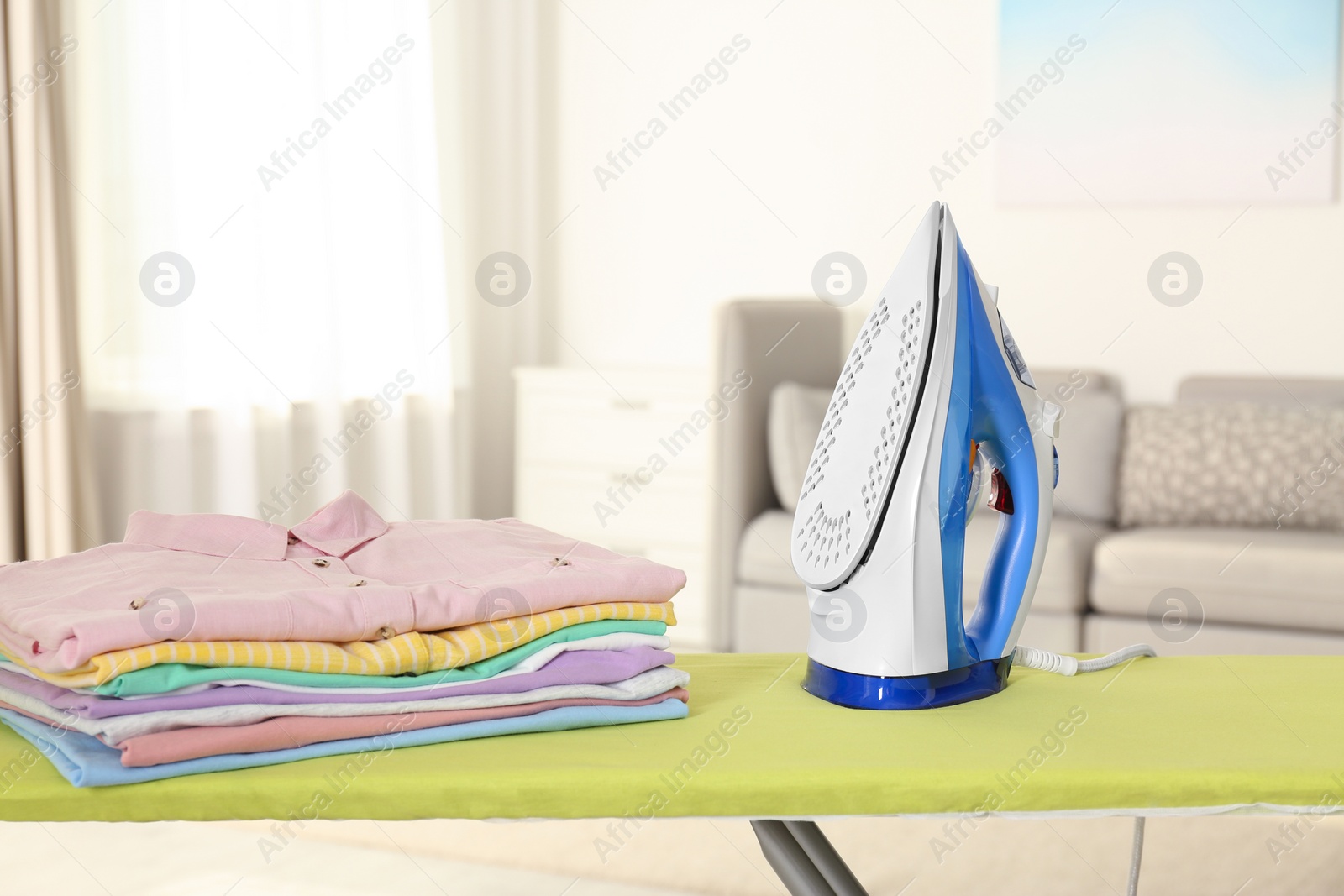 Photo of Board with modern iron and clean laundry at home