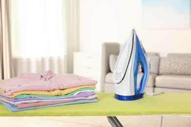 Photo of Board with modern iron and clean laundry at home