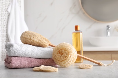 Photo of Natural loofah sponges, towels and bottle with cosmetic product on table in bathroom