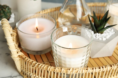 Wicker tray with burning candles and houseplant on table