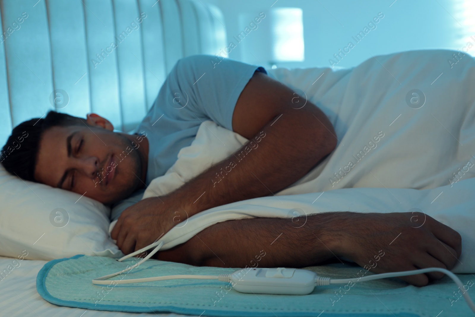 Photo of Man sleeping on electric heating pad in bed at night