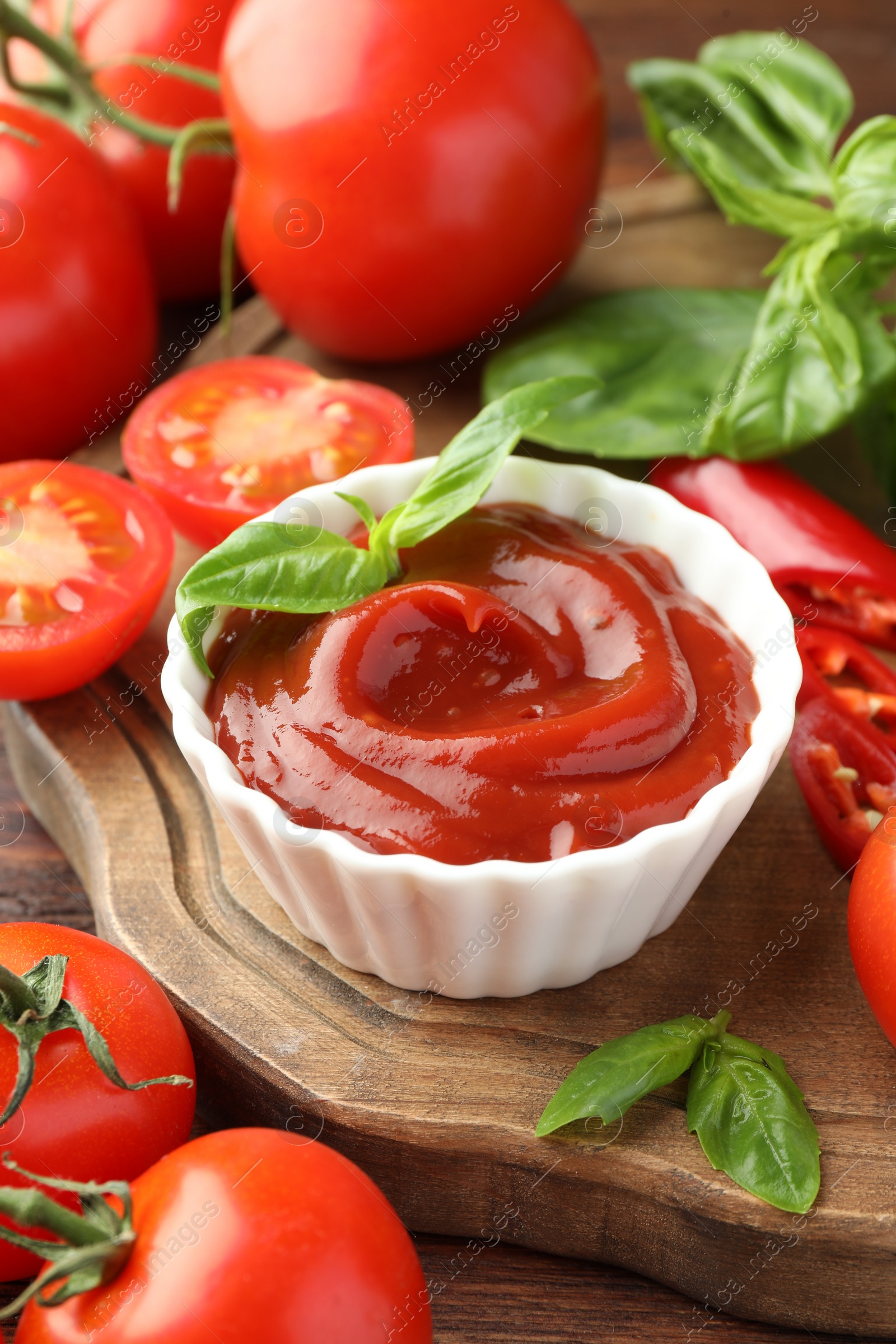 Photo of Bowl of tasty ketchup and ingredients on wooden table, closeup