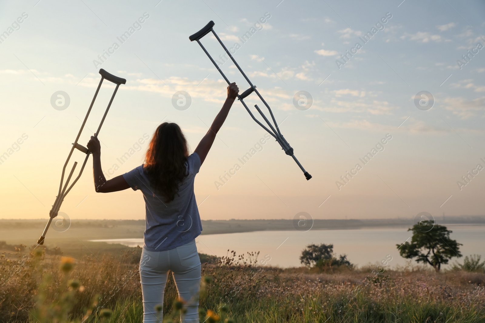 Photo of Woman holding axillary crutches outdoors at sunrise, back view. Healing miracle