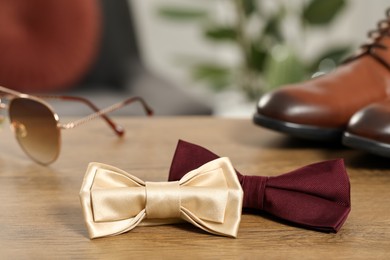 Photo of Stylish color bow ties, sunglasses and shoes on wooden table