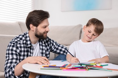 Photo of Happy dad and son drawing together at table indoors