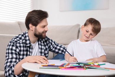 Happy dad and son drawing together at table indoors