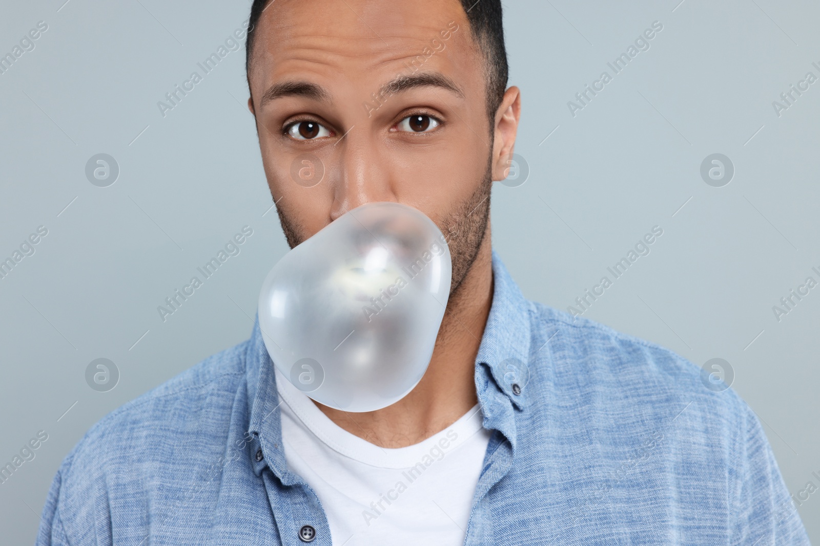 Photo of Portrait of young man blowing bubble gum on light grey background