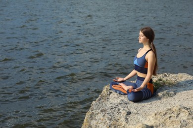 Photo of Teenage girl meditating on cliff near river. Space for text