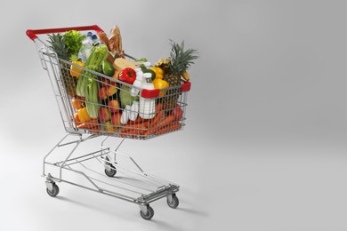 Photo of Shopping cart full of groceries on grey background. Space for text