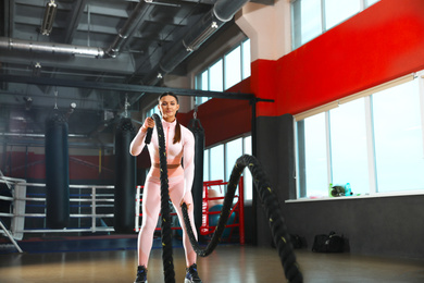 Photo of Young woman working out with battle ropes in modern gym
