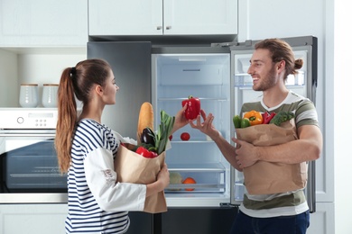 Photo of Couple with fresh products near refrigerator in kitchen