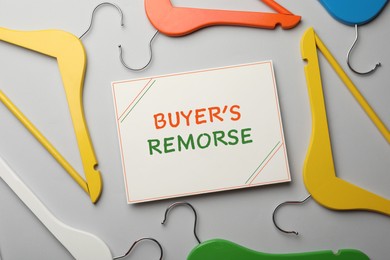 Image of Card with text Buyer's Remorse and different colorful hangers on light grey background, flat lay