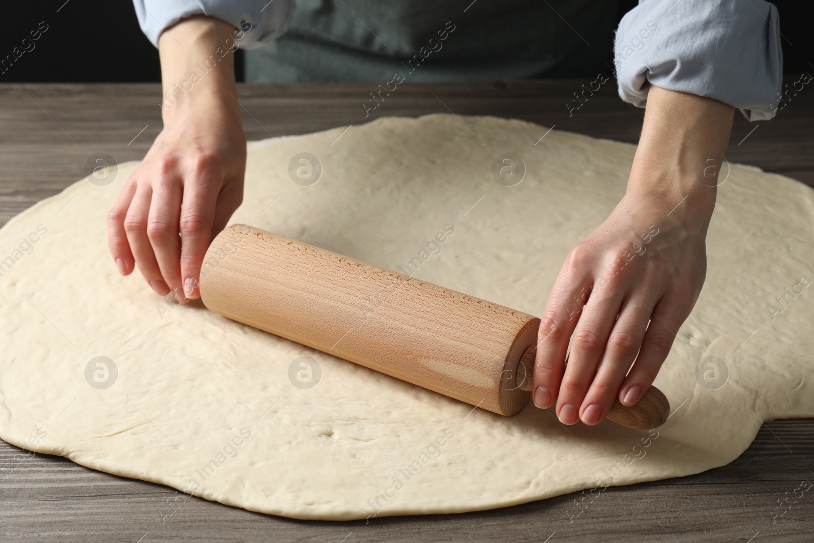 Photo of Woman rolling raw dough at wooden table, closeup