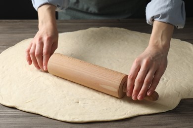 Photo of Woman rolling raw dough at wooden table, closeup