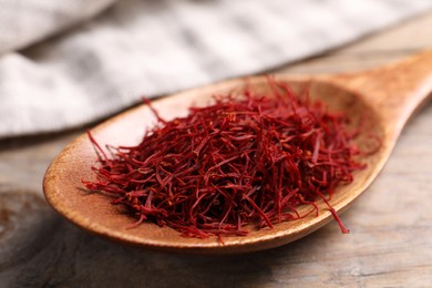 Photo of Aromatic saffron and spoon on wooden table, closeup