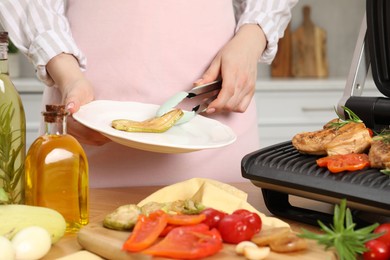 Photo of Woman cooking different products with electric grill at wooden table in kitchen, closeup