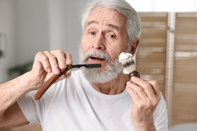 Photo of Man shaving mustache and beard with blade in bathroom