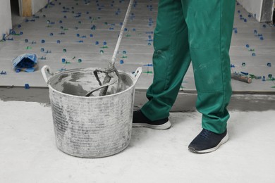 Photo of Man mixing tile adhesive indoors, closeup view