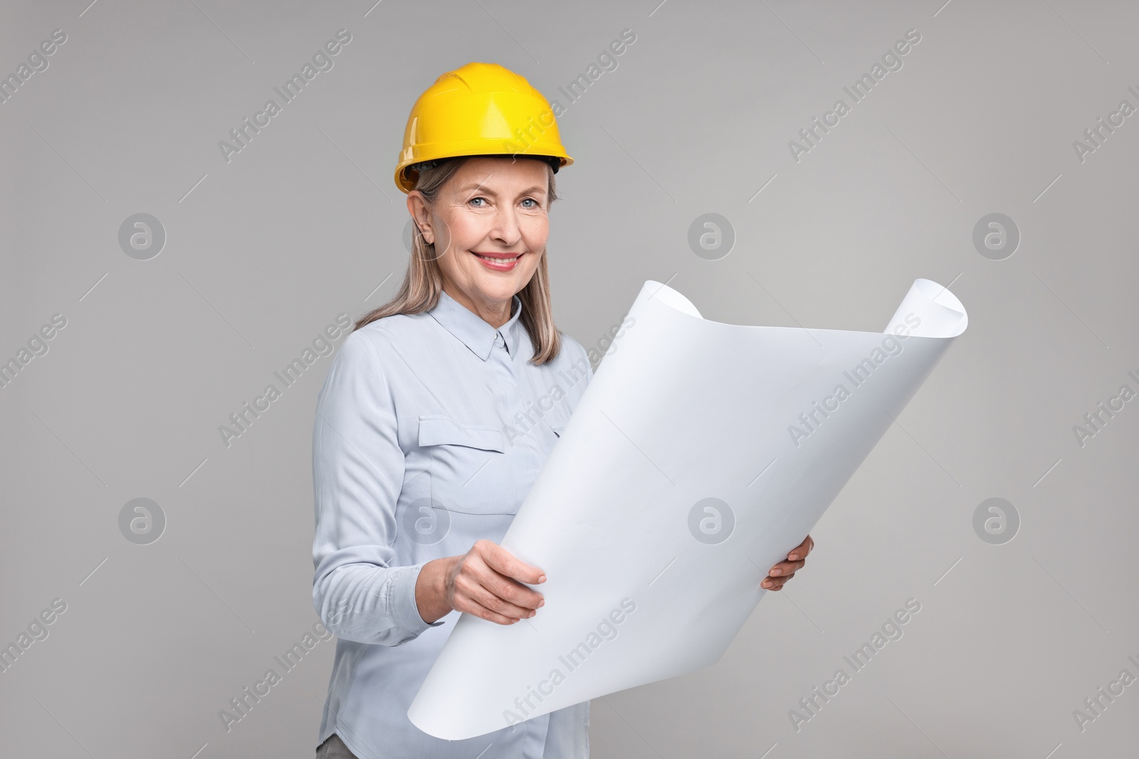 Photo of Architect in hard hat with draft on grey background
