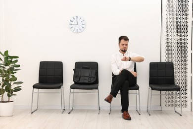 Photo of Man looking at wrist watch and waiting for job interview indoors